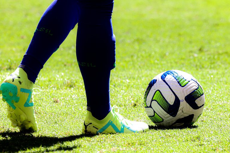 Detalhe de chuteira e bola em campo de futebol